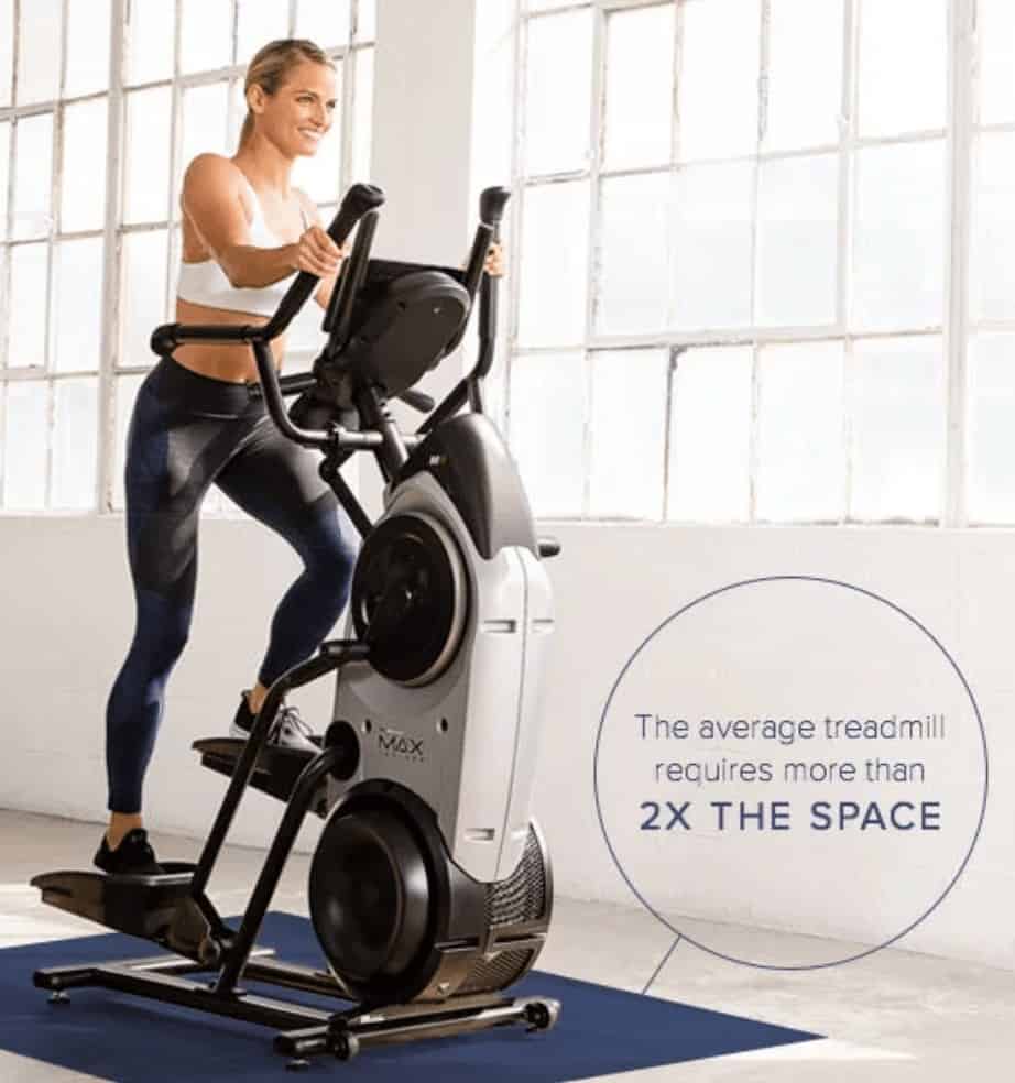 a woman rides the max trainer while showing its space saving design